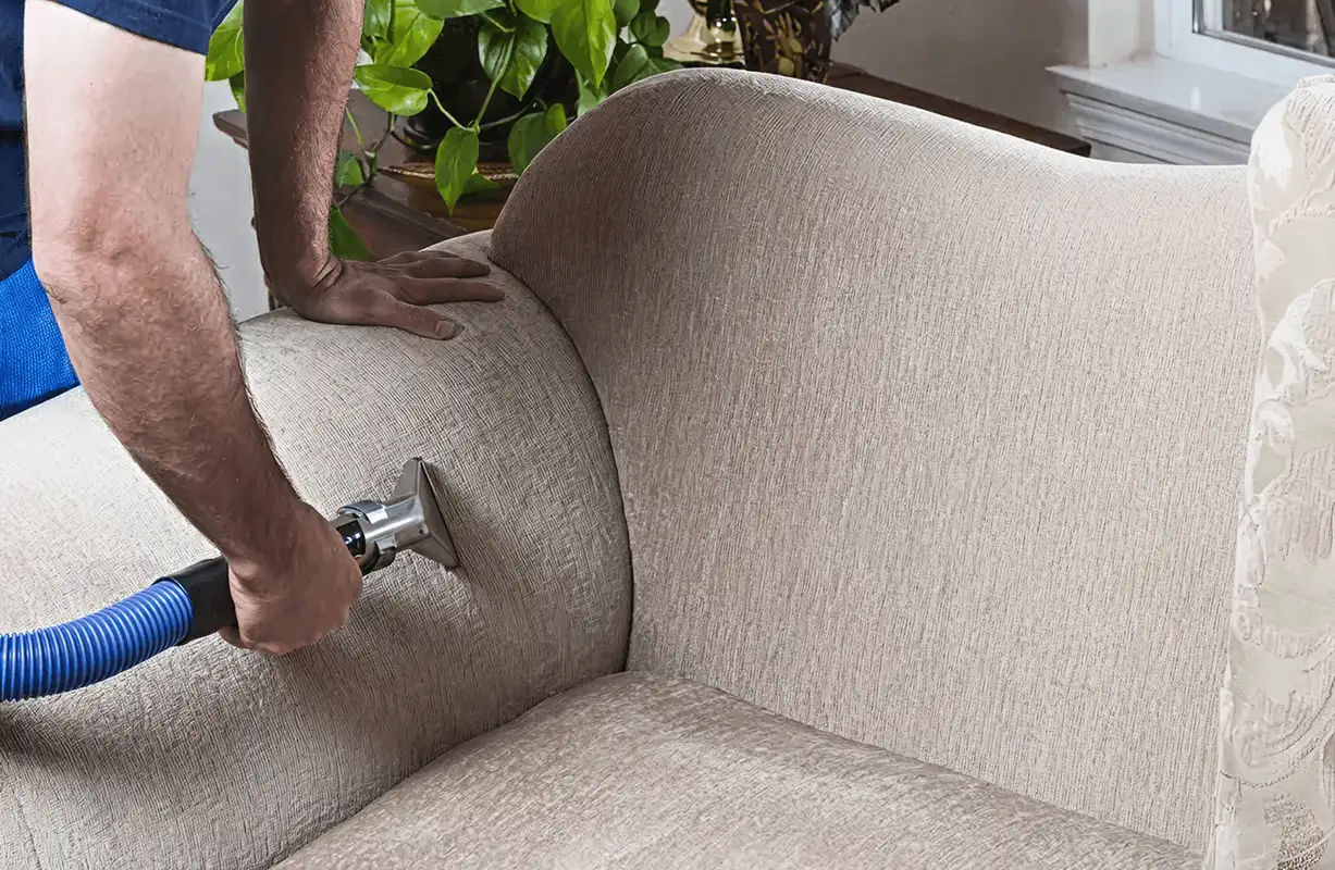 Professional upholstery cleaner deep-cleaning a fabric sofa with a handheld extraction tool and hose, Houston, TX.